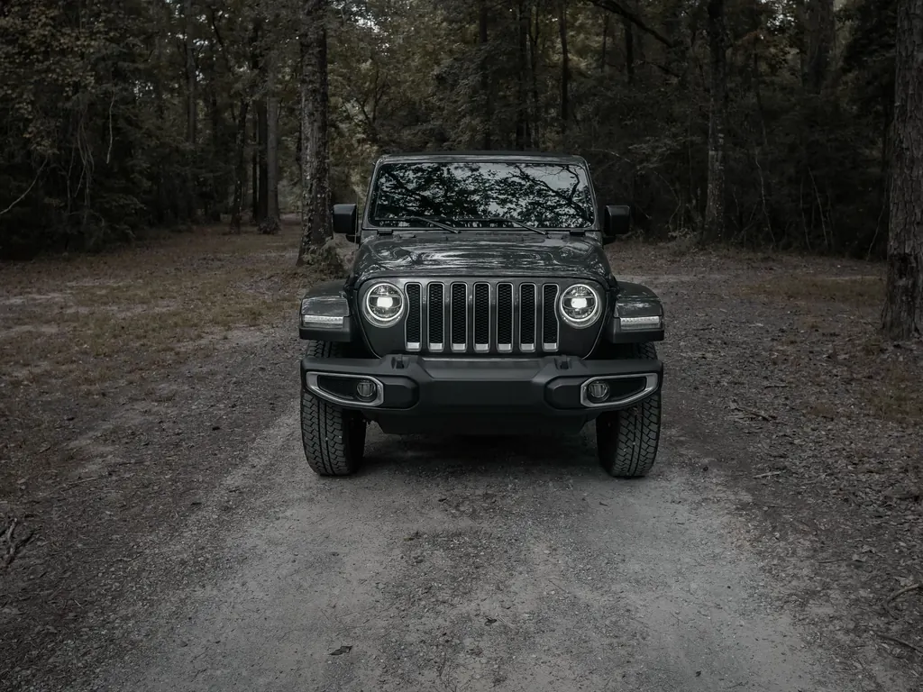 A black Jeep Wrangler with its headlights on, on a forest track